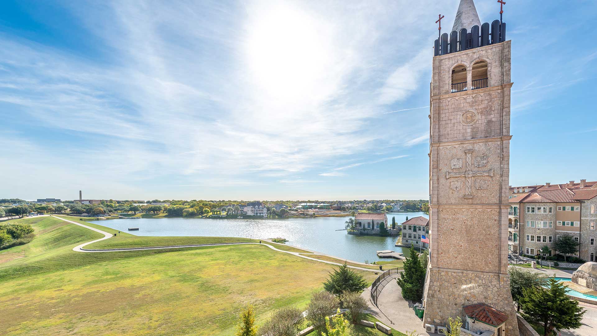 The Bell Tower stands tall on the right with an open field and the lake further beyond on the left.