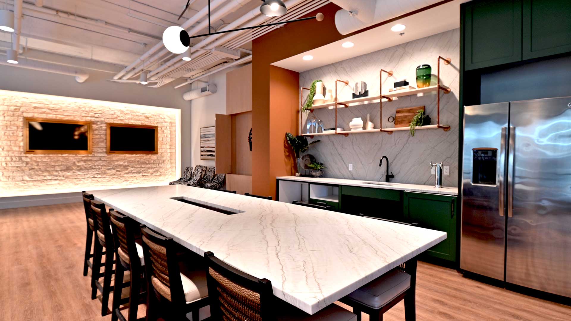 A large marble dining table sits in front of a wet bar with a large stainless steel refrigerator to the right.