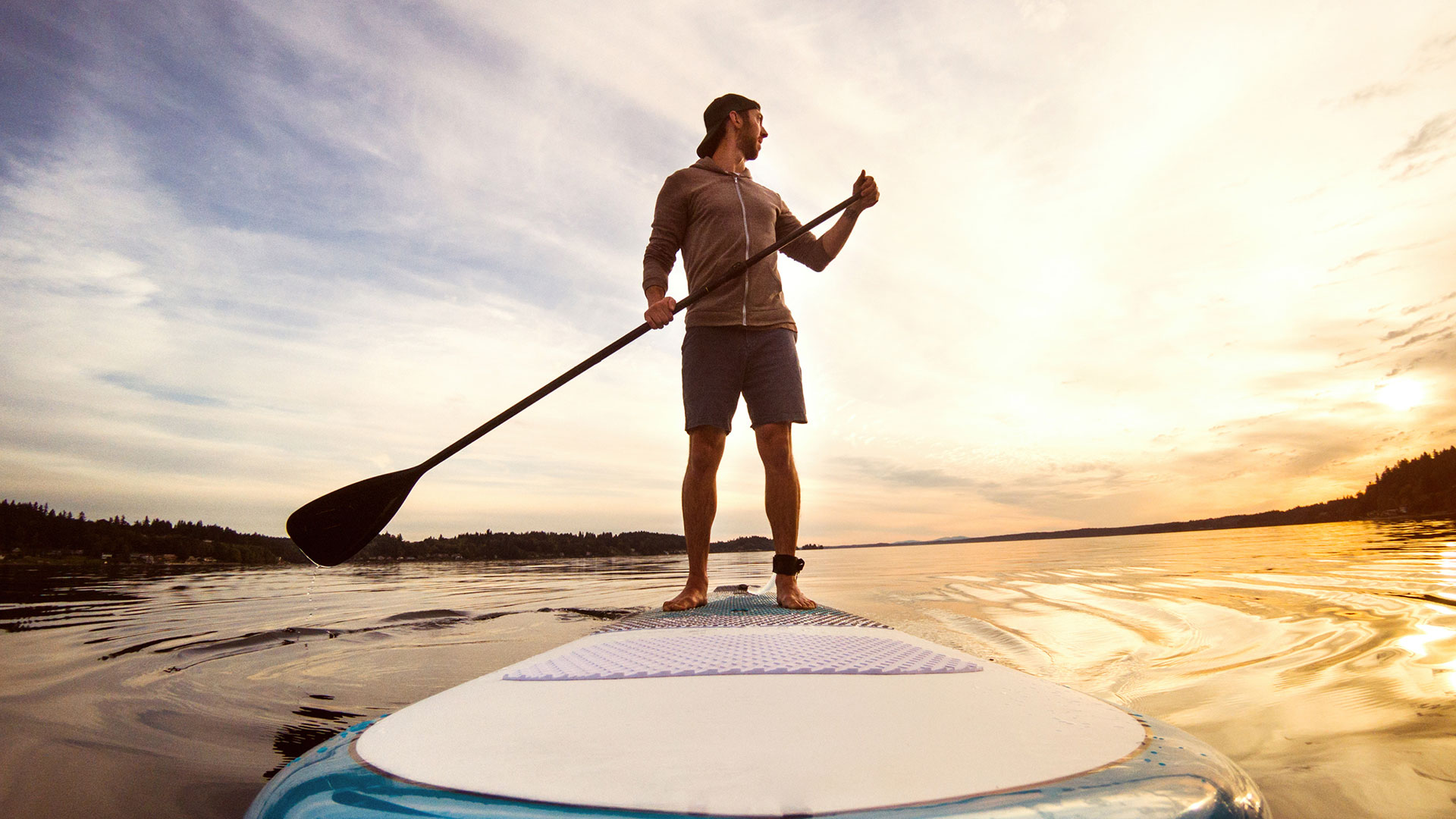 A man stands on a paddle board in the middle of a lake at sunrise.
